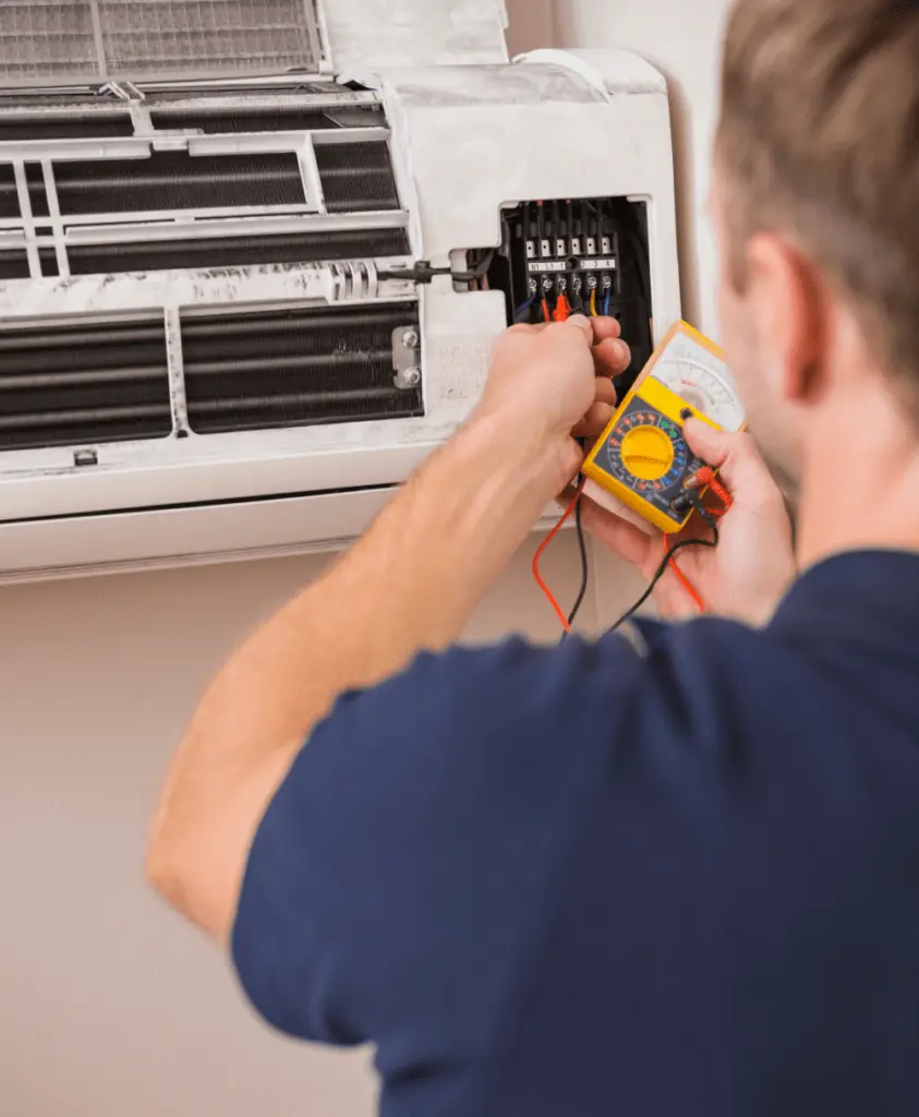 HVAC technician using a yellow multimeter to test electrical connections on a wall-mounted air conditioning unit.