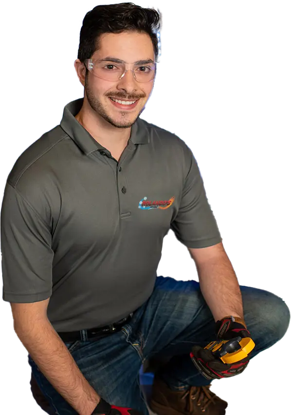 Smiling HVAC technician wearing safety glasses and gloves, holding a diagnostic tool, dressed in a Rolando's HVAC uniform.
